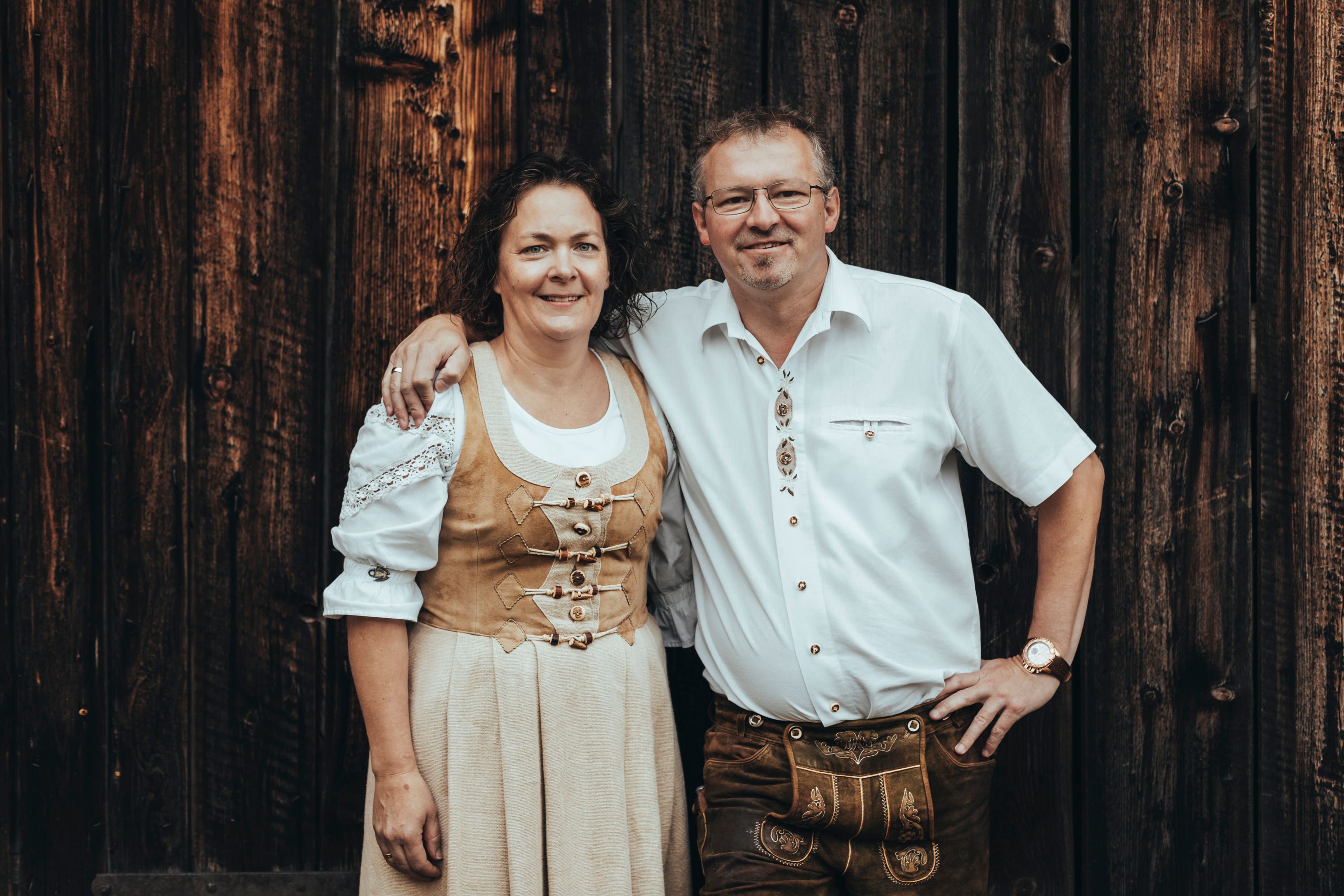 Ein Mann und eine Frau in traditioneller Tracht vor einer Holzwand.