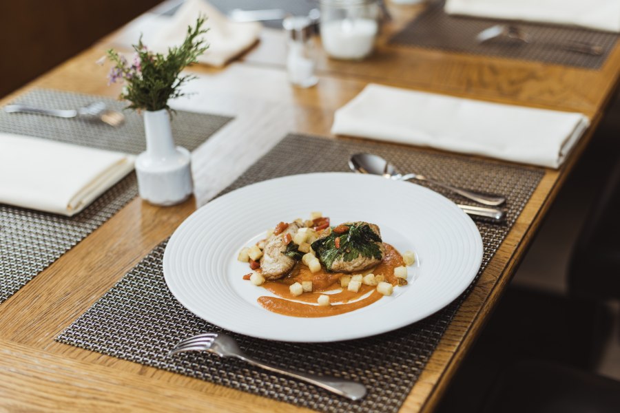 Elegantes Gericht auf weißem Teller, dekorativ angerichtet auf Holztisch.