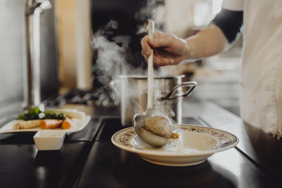 Eine Person sch&ouml;pft Suppe mit einem Kn&ouml;del aus einem Topf in einen Teller.