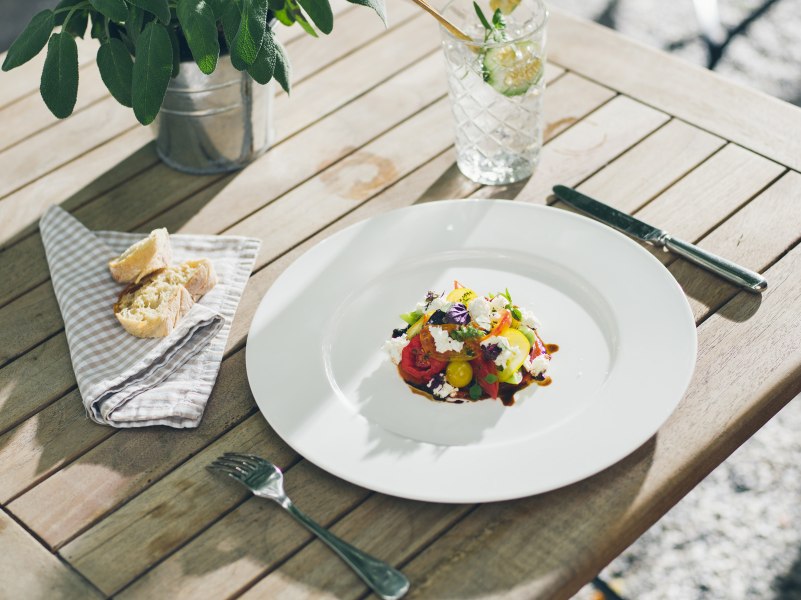 Elegantes Gericht auf einem wei&szlig;en Teller mit Brot und Getr&auml;nk auf Holztisch.