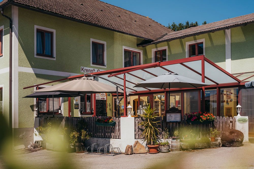 Außenansicht eines Wirtshauses mit Terrasse und Sonnenschirmen.
