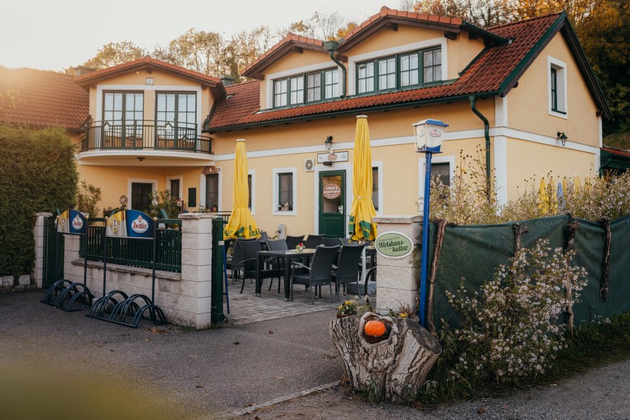 Gasthaus mit Terrasse, gelben Sonnenschirmen und Blumendekor.