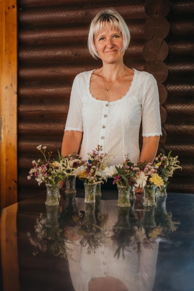 Eine Frau in wei&szlig;er Bluse steht hinter einem Tisch mit Blumenvasen.