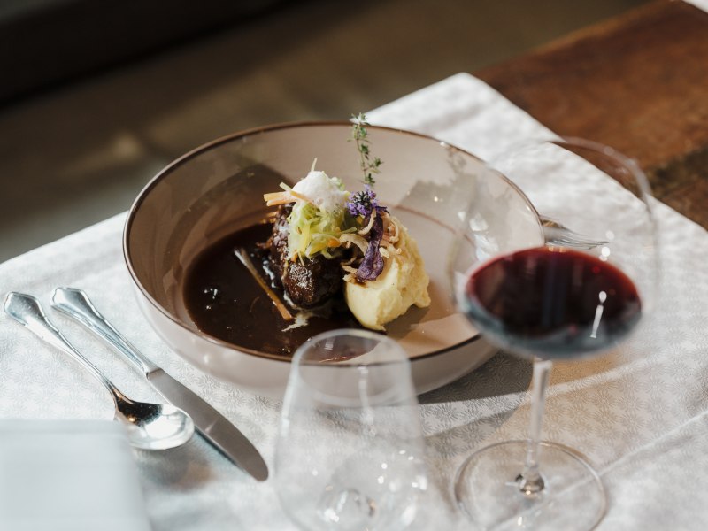 Gourmetgericht mit Fleisch, Kartoffelp&uuml;ree und Rotwein auf gedecktem Tisch.