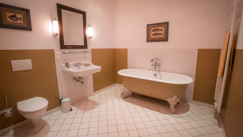 Elegantes Badezimmer mit freistehender Badewanne, Waschbecken, Spiegel und WC. W&auml;nde in Beige und Wei&szlig;, dekoriert mit Fischbildern.