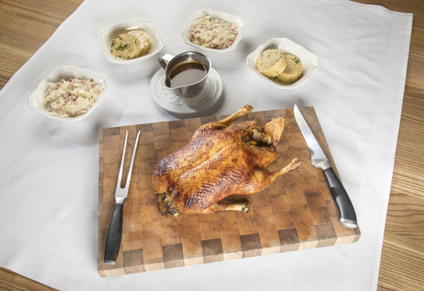 Gebackene Ente auf einem Holzbrett mit Beilagen und Soße.