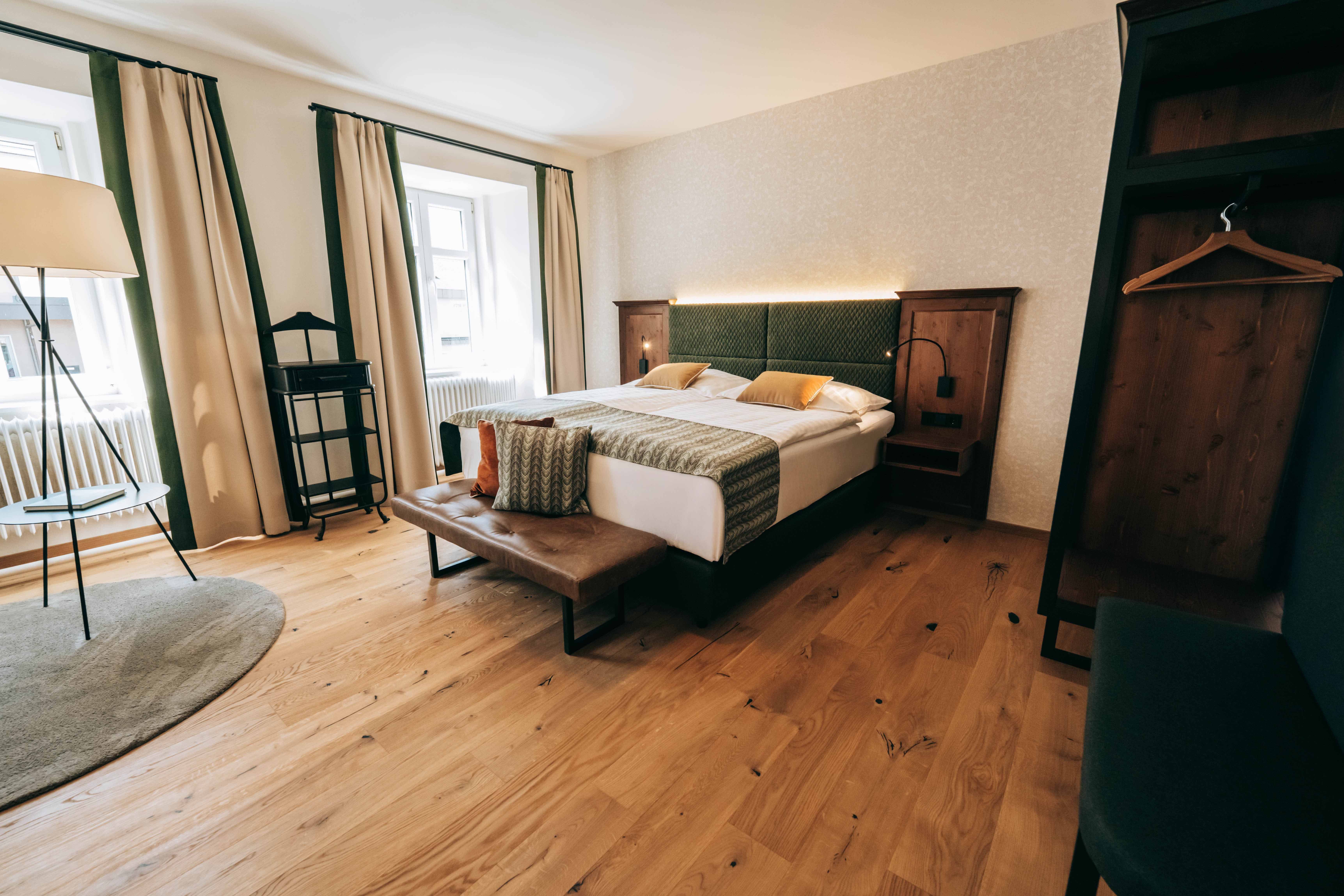 Modern eingerichtetes Hotelzimmer mit Doppelbett, Holzboden und großen Fenstern.