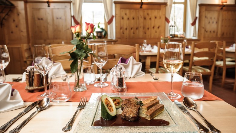 Ein elegant gedeckter Tisch in einem rustikalen Restaurant mit einem Teller Gourmet-Essen, Weingl&auml;sern und einer Vase mit Rosen.