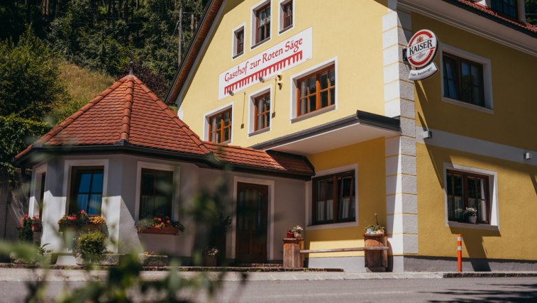Gelbes Gebäude mit der Aufschrift 'Gasthof zur Roten Säge' und einem Kaiser-Bierschild.