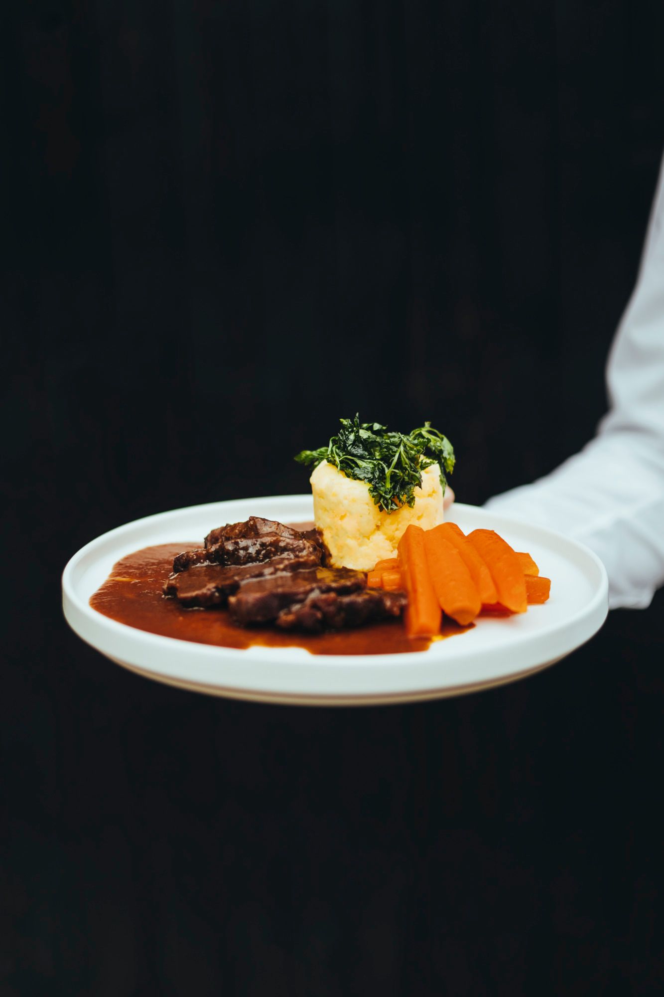 Gourmetgericht mit Fleisch, Karotten und Erdäpfelstampf auf weißem Teller.