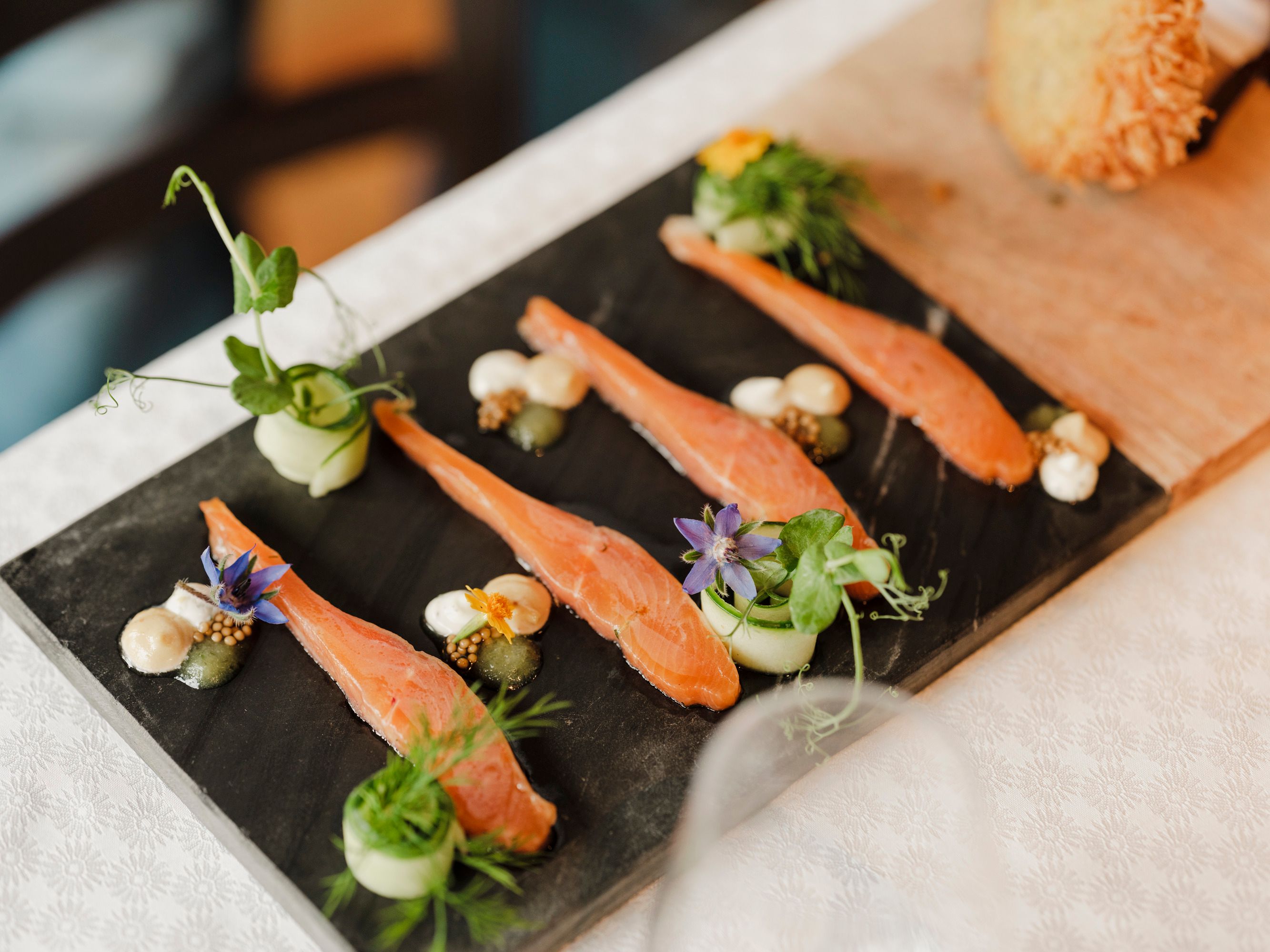 Gourmetgericht mit Lachs, Kräutern und Blüten auf Schieferplatte serviert.