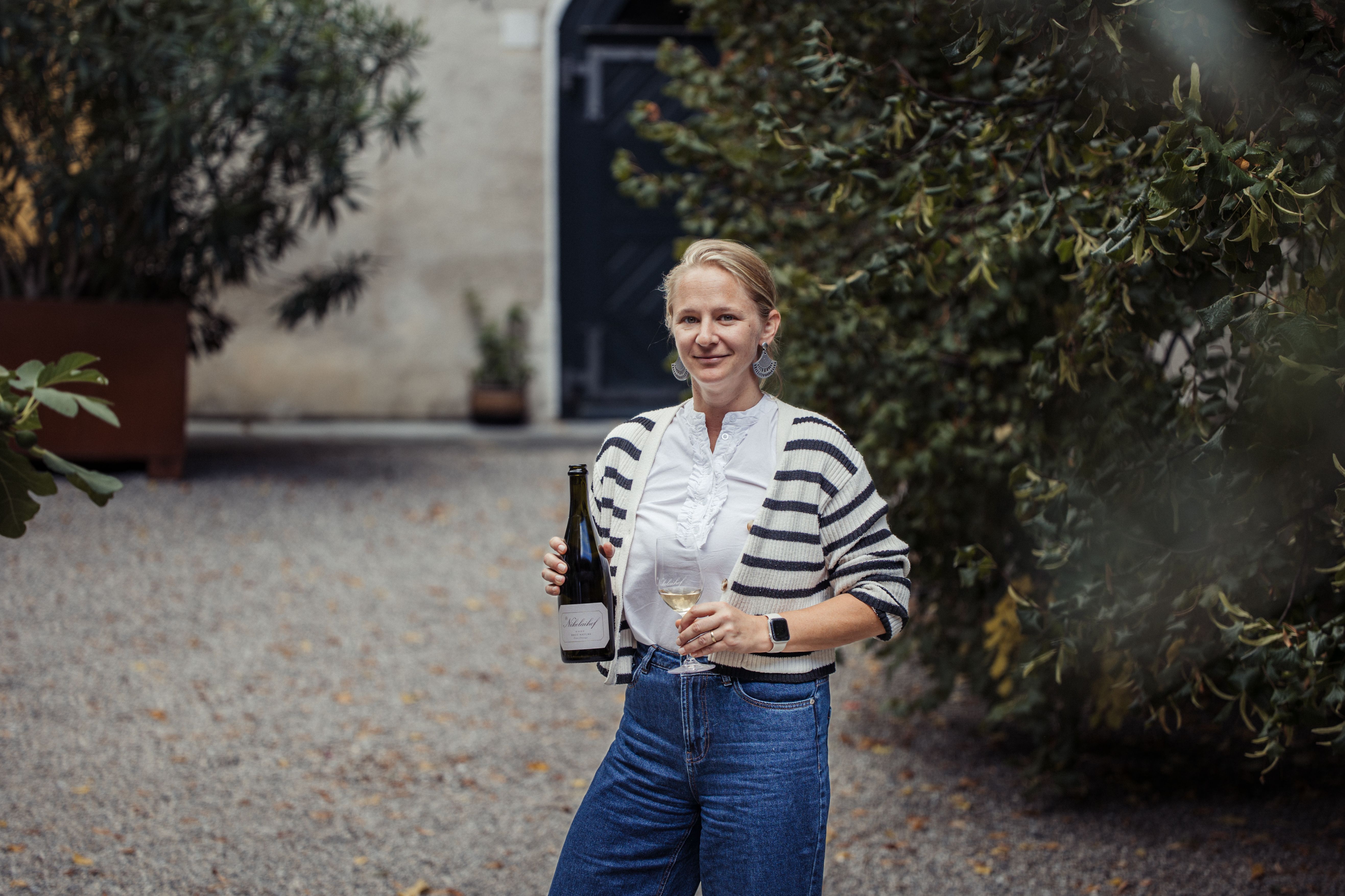Eine Frau steht im Freien mit einer Weinflasche und einem Glas Wein in der Hand.