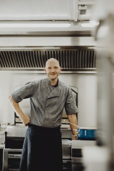 Ein Koch in einer professionellen K&uuml;che, l&auml;chelnd in die Kamera schauend.