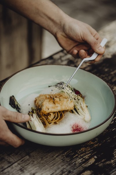Ein Teller mit gebackenem Fisch auf Nudeln, garniert mit Sprossen und Gemüse.