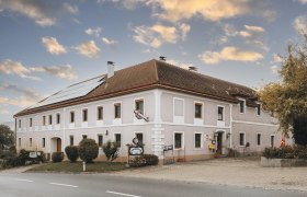 Ein traditioneller Landgasthof mit Solarpanelen auf dem Dach und einem Schild vor dem Eingang, unter einem bew&ouml;lkten Himmel.