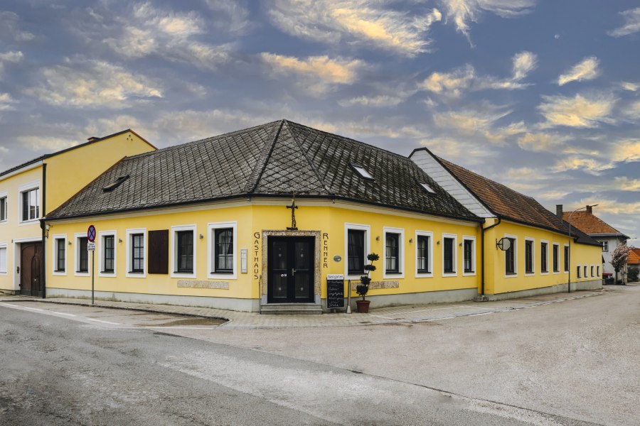 Gelbes Gasthaus an Stra&szlig;enecke mit bew&ouml;lktem Himmel im Hintergrund.