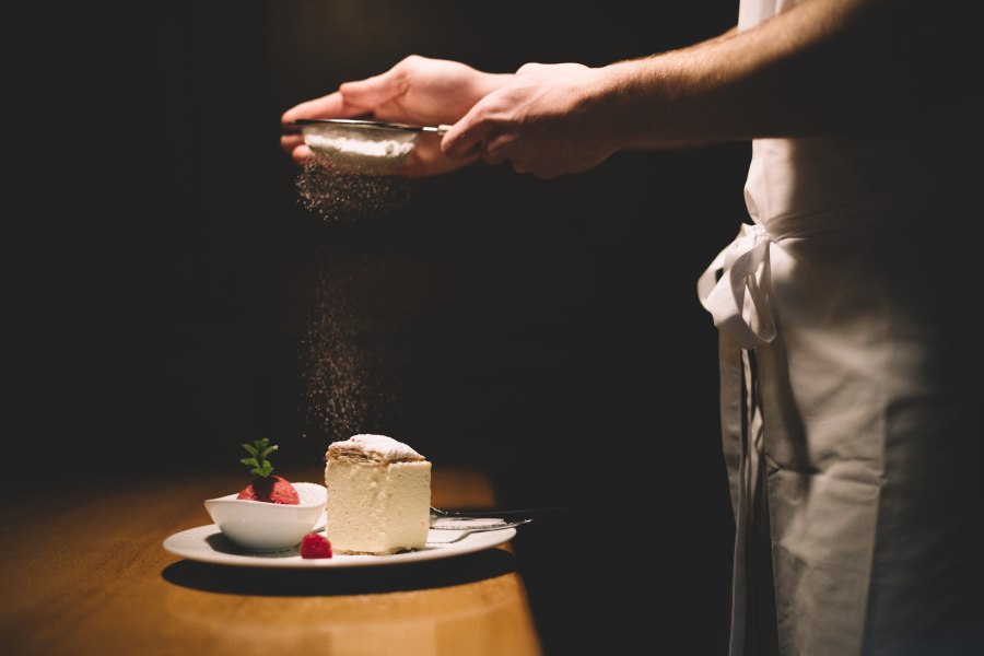 Ein Teller mit Cremeschnitte und Himbeersorbet, dar&uuml;ber wird Puderzucker gestreut.