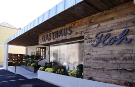 Au&szlig;enansicht des Gasthauses Josef Floh mit Holzwand und Pflanzen.
