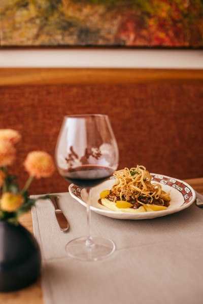 Ein Teller mit glasierter Kalbsleber auf Kartoffelp&uuml;ree, garniert mit R&ouml;stzwiebeln, neben einem Glas Rotwein auf einem Tisch.
