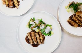 Drei Teller mit kunstvoll angerichteten Gourmetgerichten auf wei&szlig;em Tischtuch.