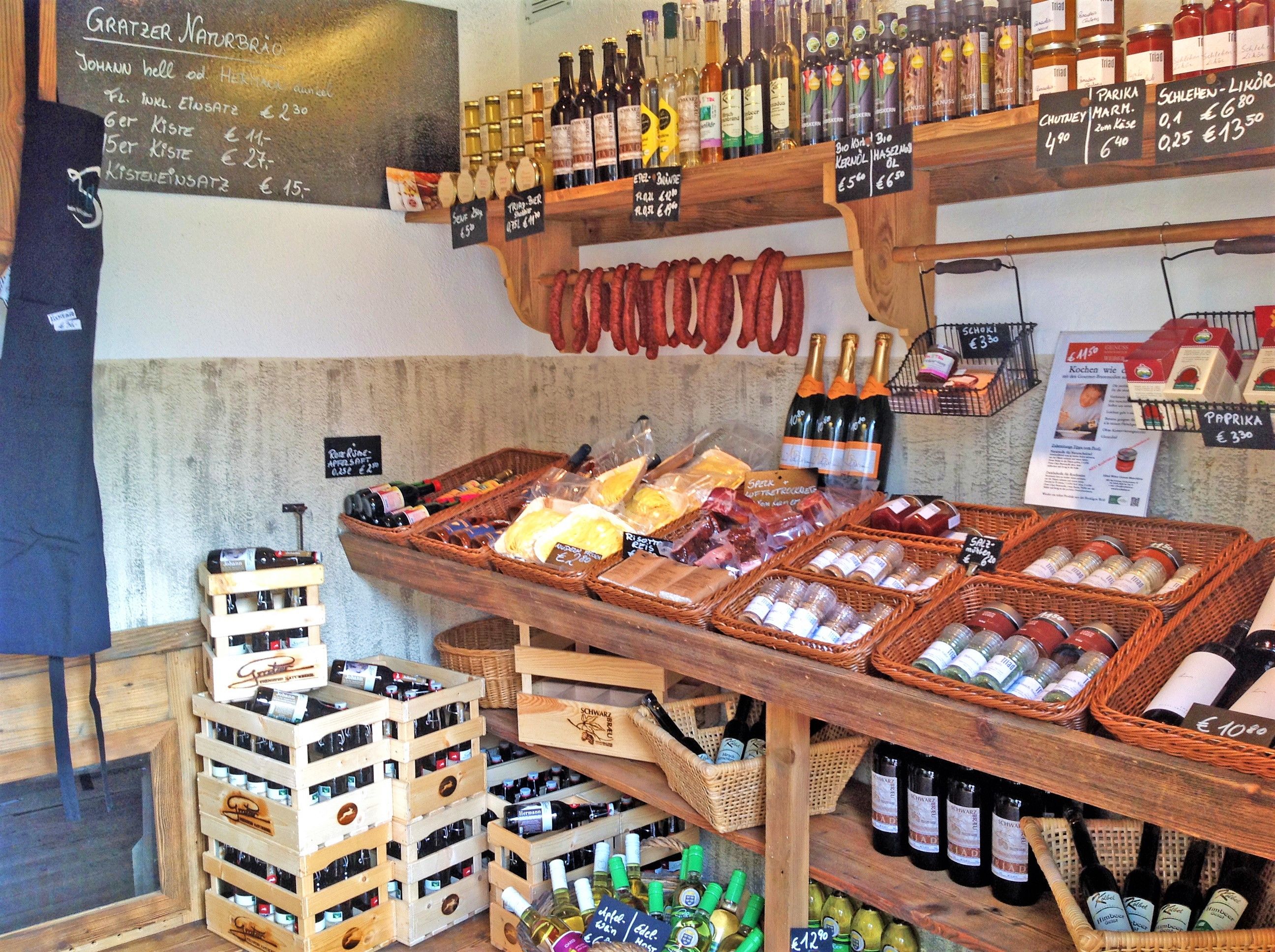 Innenansicht eines Hofladens mit Regalen voller regionaler Produkte wie Wein, Wurst, Gewürze und Öl.