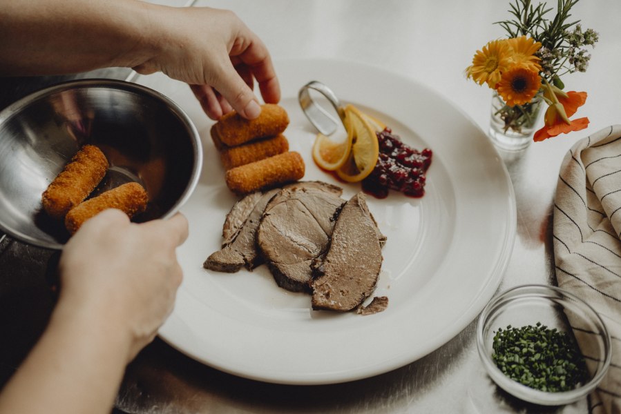 Ein Teller mit Fleisch, Kroketten, Preiselbeeren und Zitronenscheiben wird angerichtet.