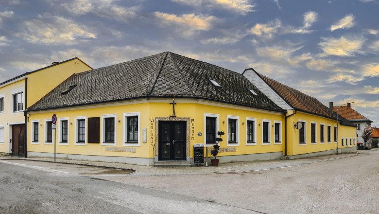 Gelbes Gasthaus an Stra&szlig;enecke mit bew&ouml;lktem Himmel im Hintergrund.
