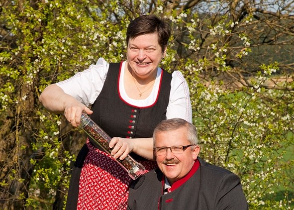 Ein Mann und eine Frau in traditioneller Kleidung lächeln im Freien, die Frau hält eine große Pfeffermühle.