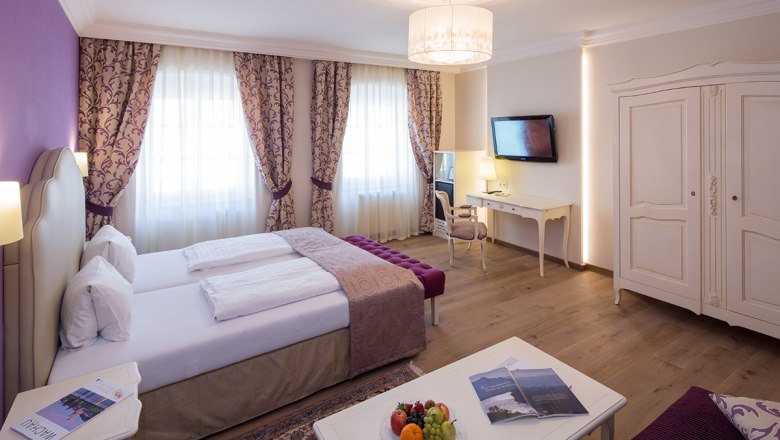Elegantes Hotelzimmer mit Doppelbett, Schreibtisch, TV und Obstteller.
