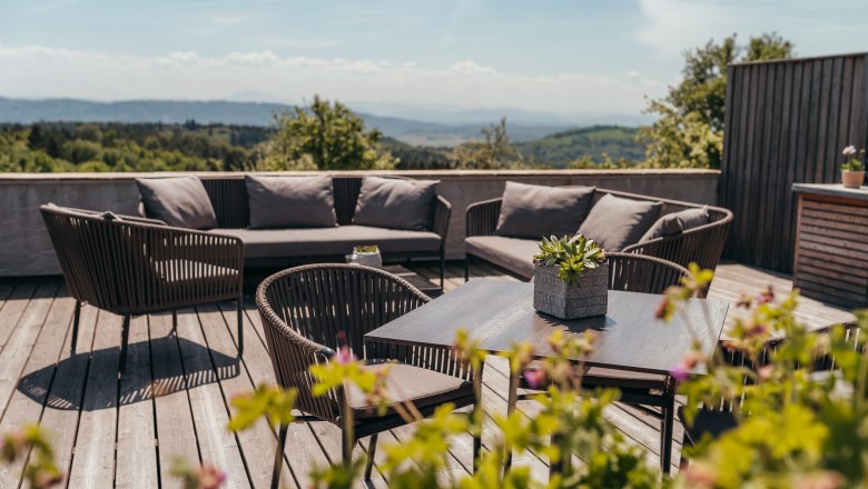 Terrasse mit Sitzmöbeln und Pflanzen, im Hintergrund eine weite Landschaft.