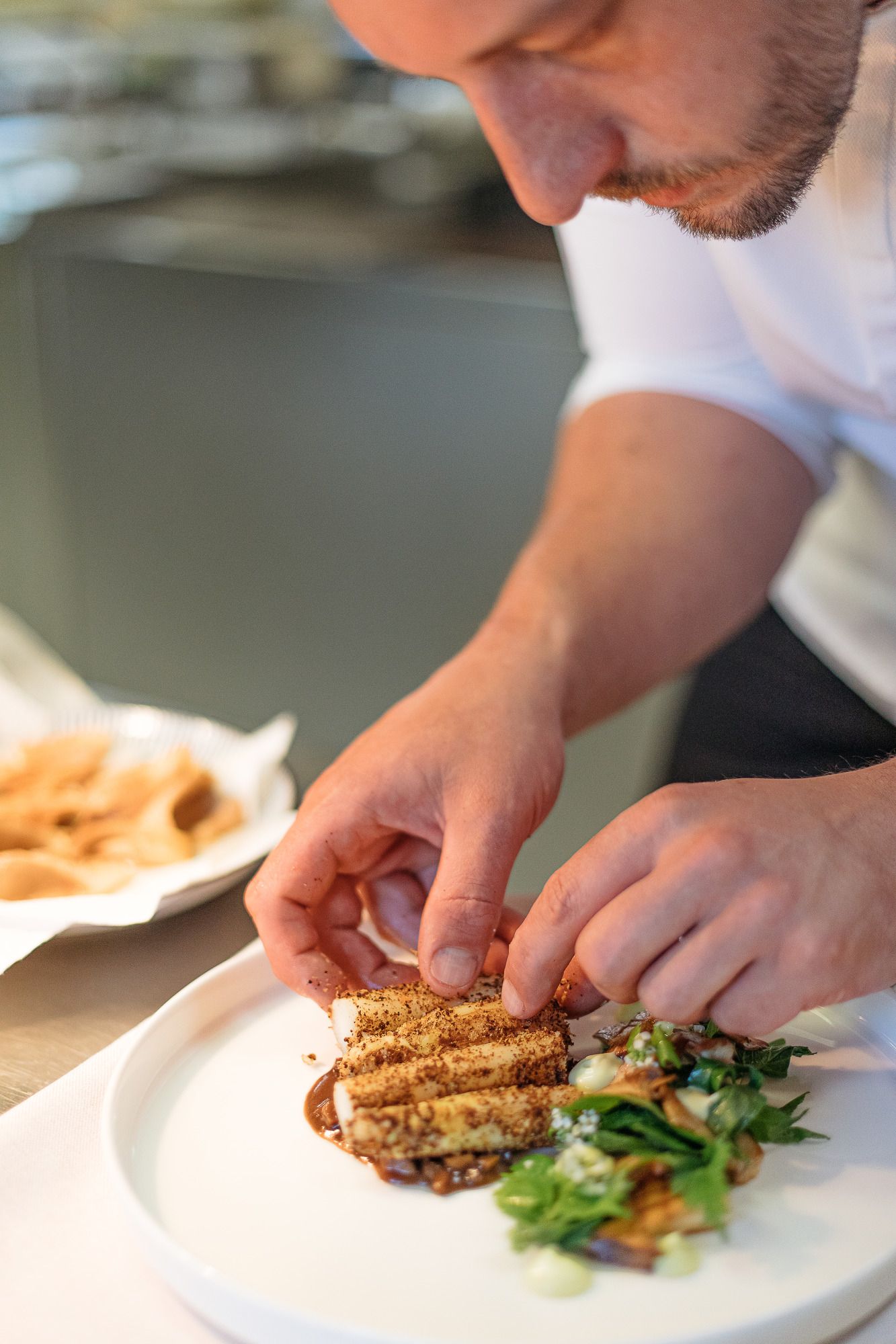 Ein Koch richtet ein kunstvolles Gericht auf einem weißen Teller an.