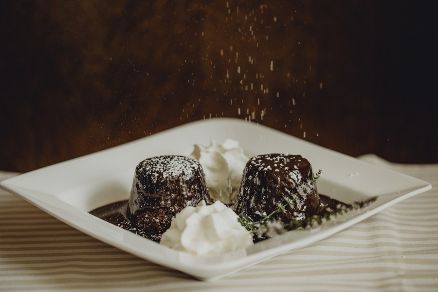 Zwei Schokoladenk&uuml;chlein mit Puderzucker und Sahne auf einem Teller.