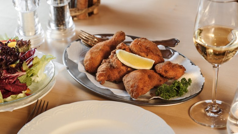 Ein Teller mit paniertem H&auml;hnchen, Salat und einem Glas Wei&szlig;wein auf einem Tisch.