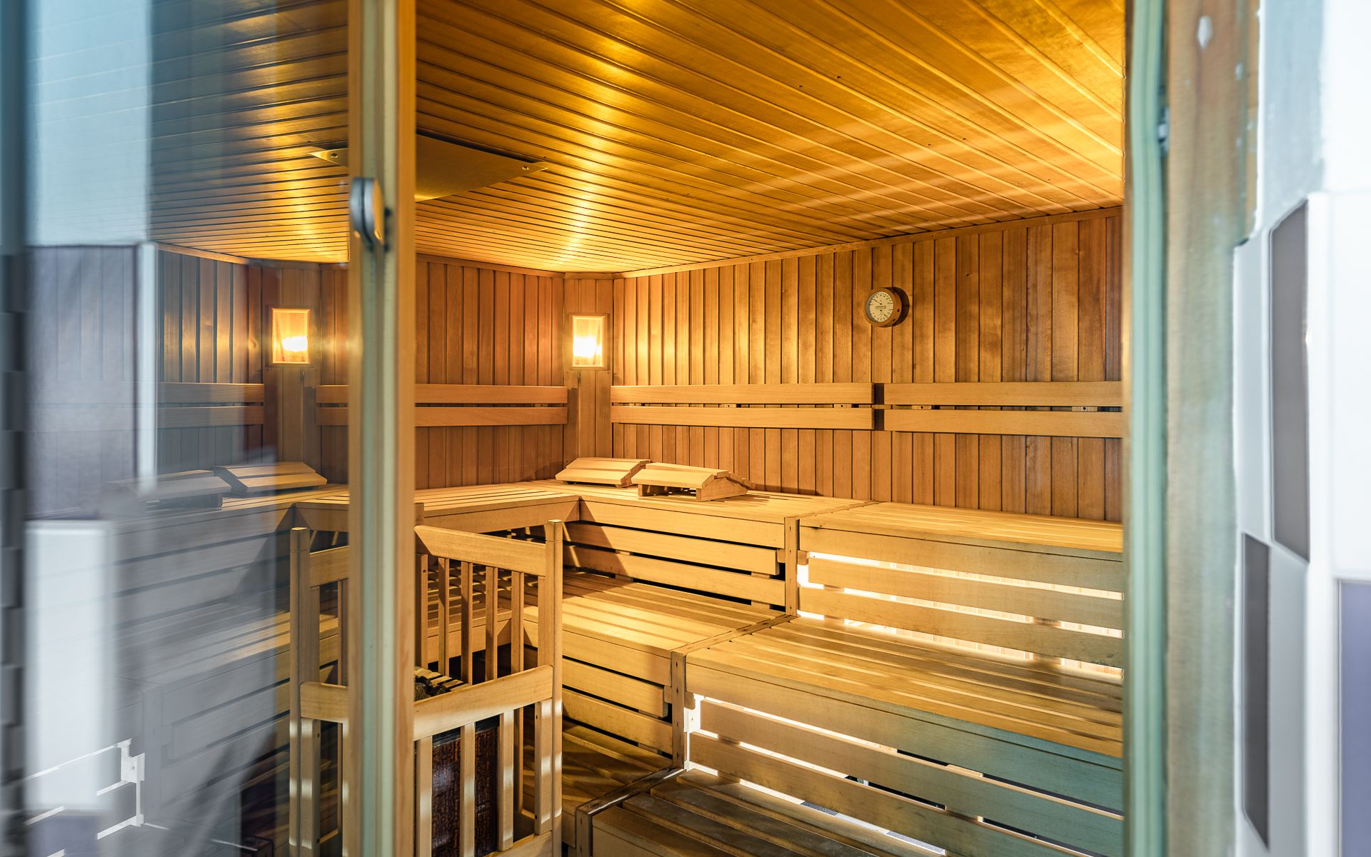 Innenansicht einer leeren Sauna mit Holzbänken und Wanduhr.