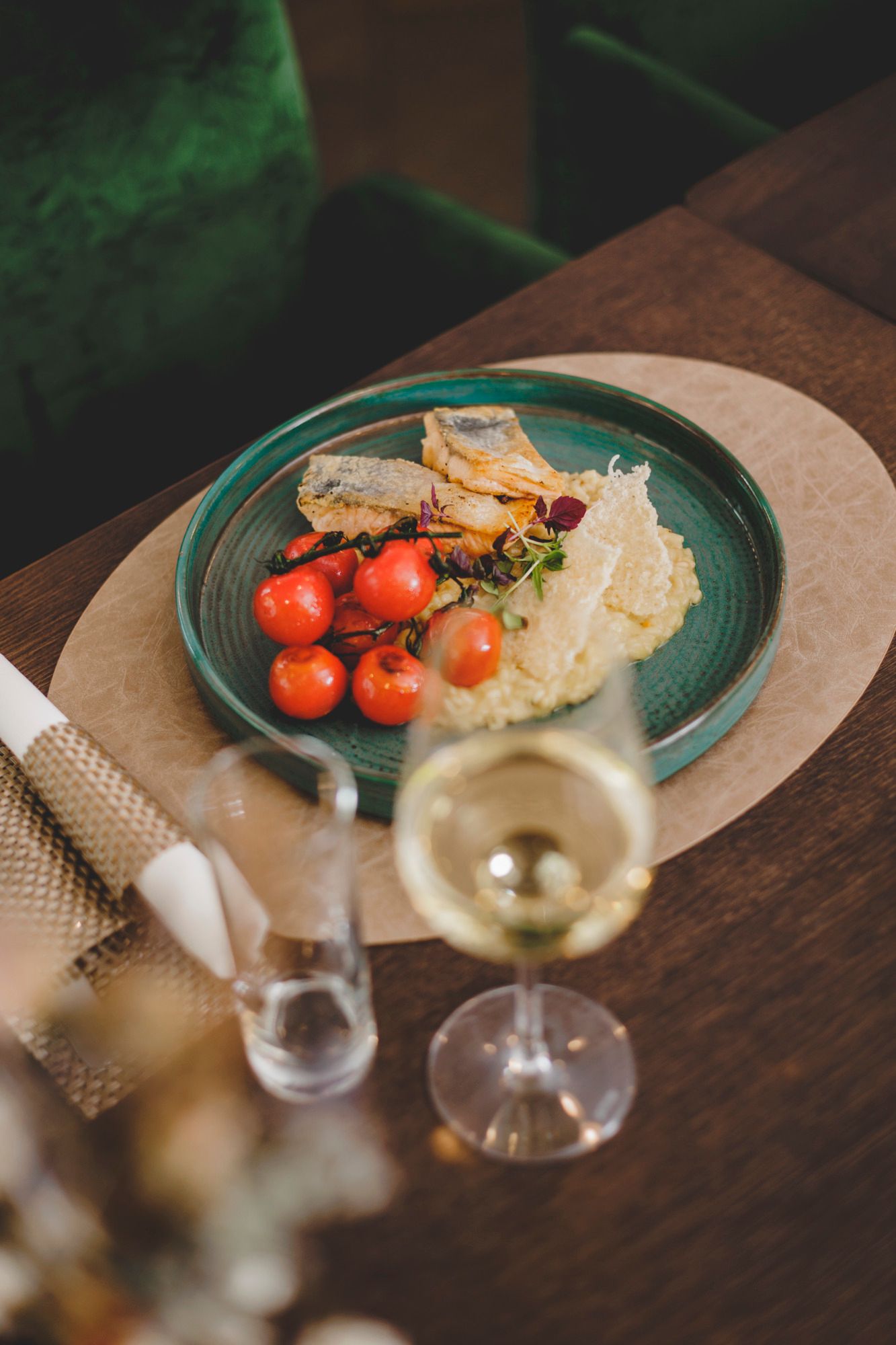 Ein Teller mit gegrilltem Fischfilet, Zitronenrisotto und Kirschtomaten, daneben ein Glas Weißwein.