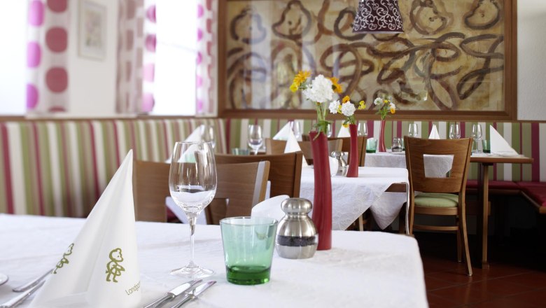 Innenansicht eines stilvoll gedeckten Restaurants mit wei&szlig;en Tischdecken, Blumenvasen und Kunst an der Wand.