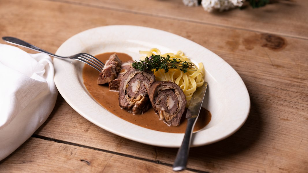 Gerollter Rostbraten mit Schwammerlfülle und Nudeln auf einem Teller.