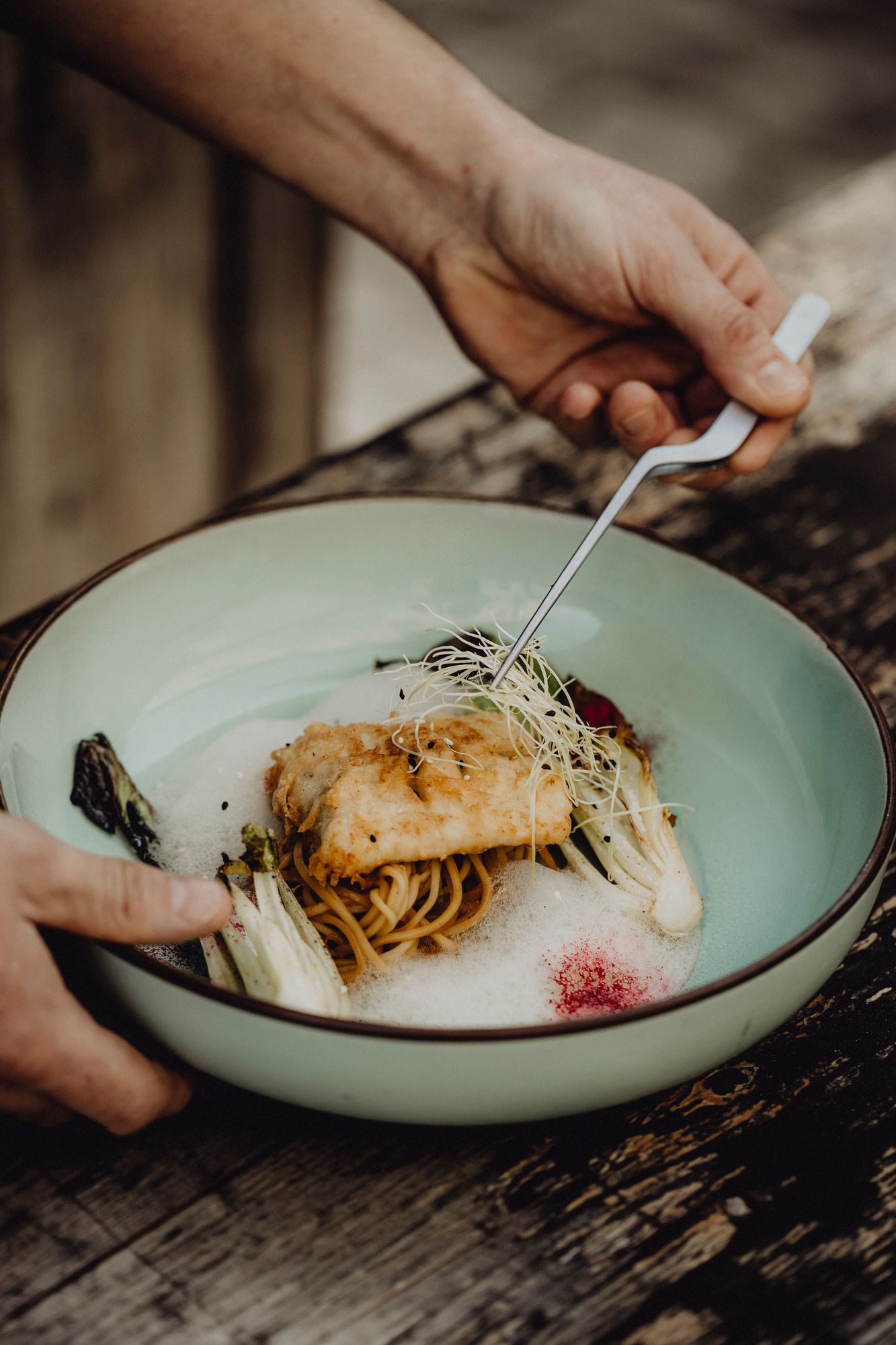 Ein Teller mit gebackenem Fisch auf Nudeln, garniert mit Sprossen und Gemüse.