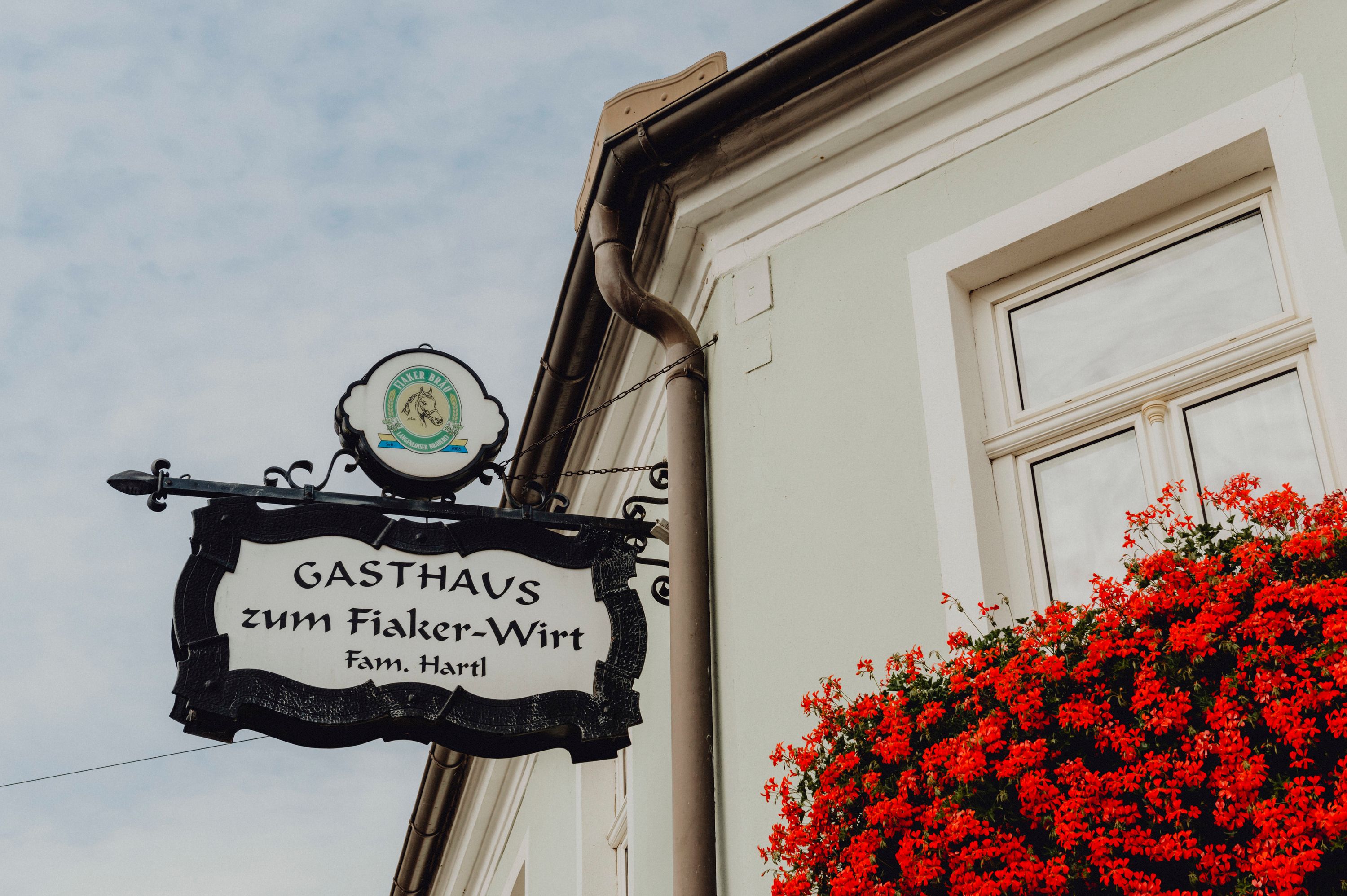 Schild des Gasthauses zum Fiaker-Wirt in Langenlois mit roten Blumen am Fenster.