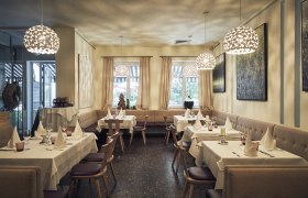 Elegantes Restaurant mit gedeckten Tischen, modernen Lampen und Kunst an den W&auml;nden.