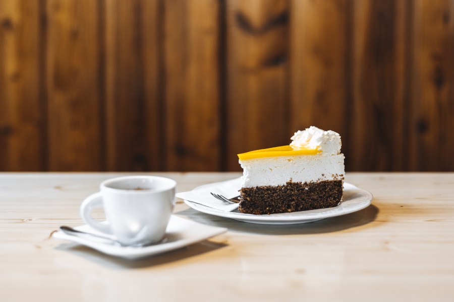 St&uuml;ck Kuchen mit Sahne und Tasse Kaffee auf Holztisch.