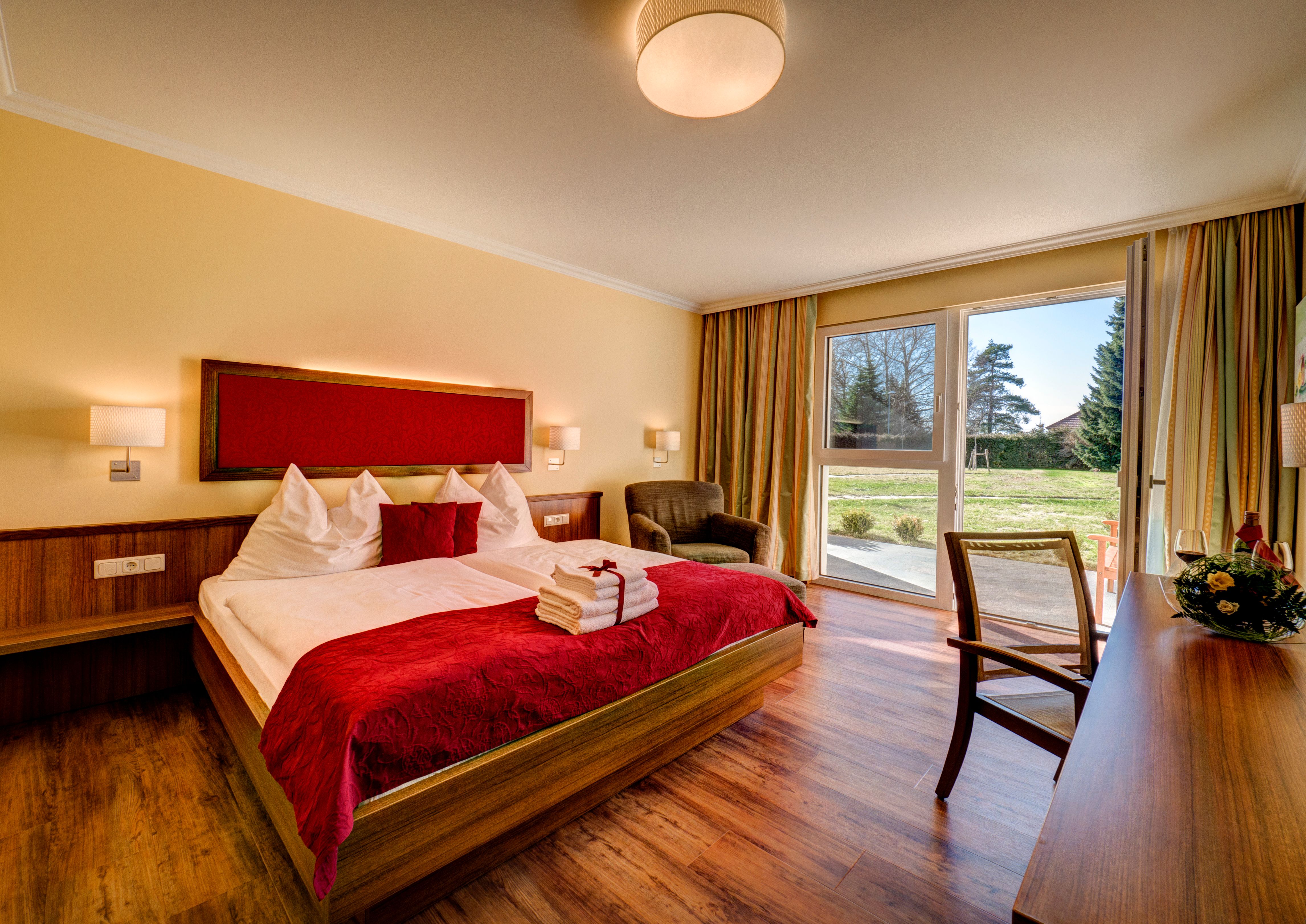 Cozy hotel room with double bed, red accents and a view of the garden through large windows.