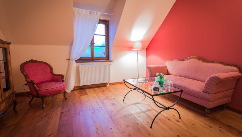 Gem&uuml;tliches Wohnzimmer mit rotem Sofa, Sessel, Glastisch und Stehlampe vor roter Wand.