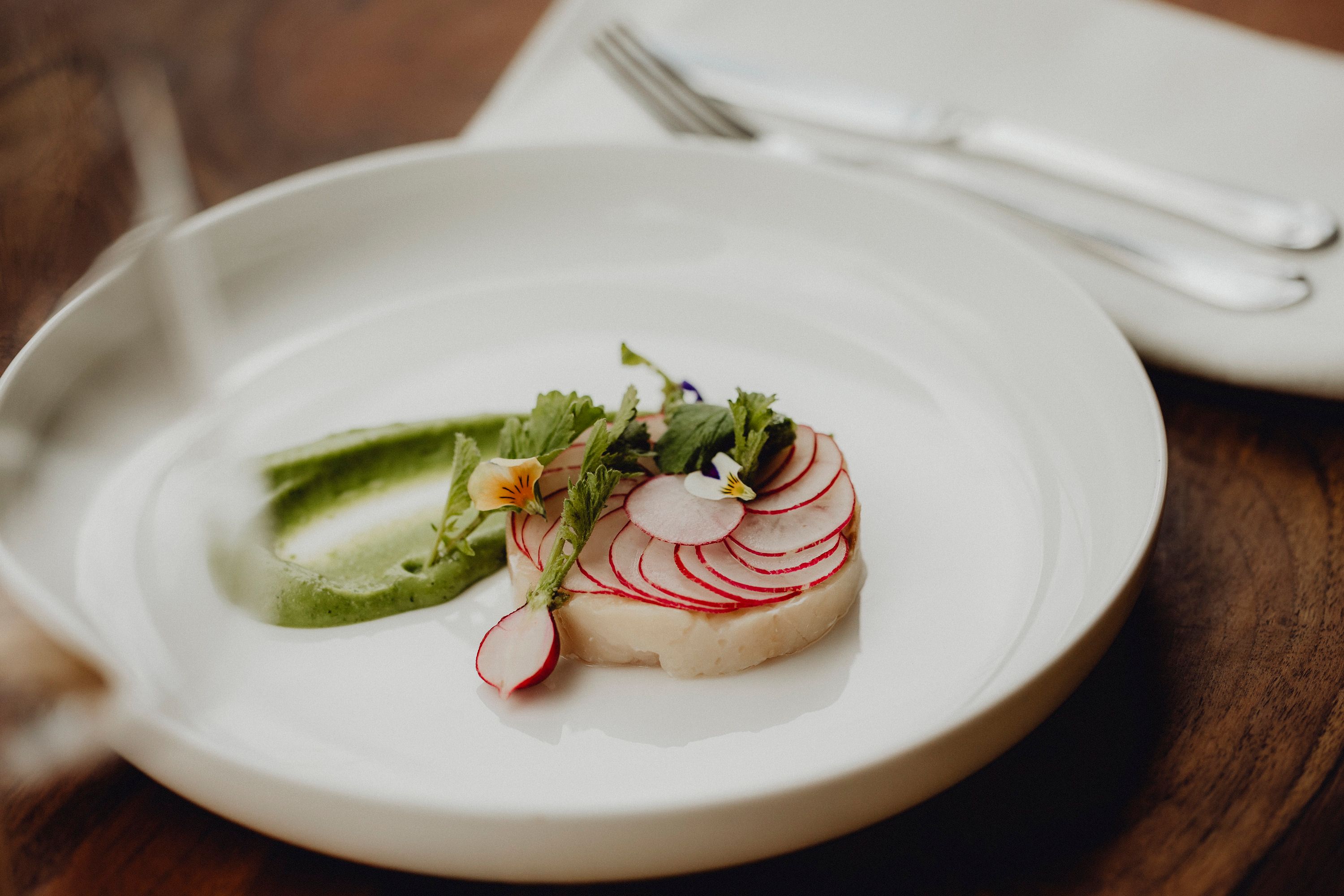 Ein Tellergericht mit Saibling, Radieschen und Wasabi-Creme, dekoriert mit essbaren Blüten.