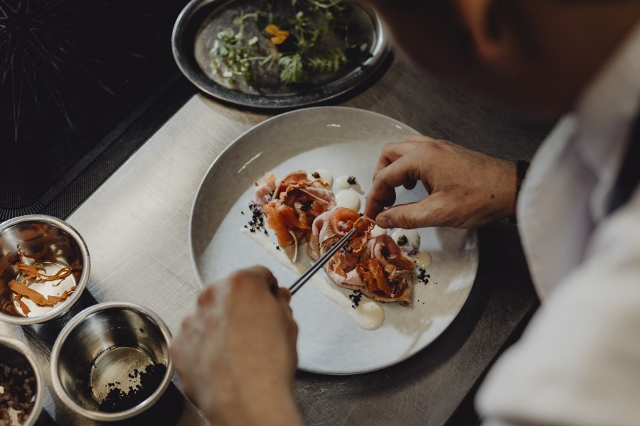 Koch dekoriert ein Gericht mit Lachs und Gemüse auf einem Teller.