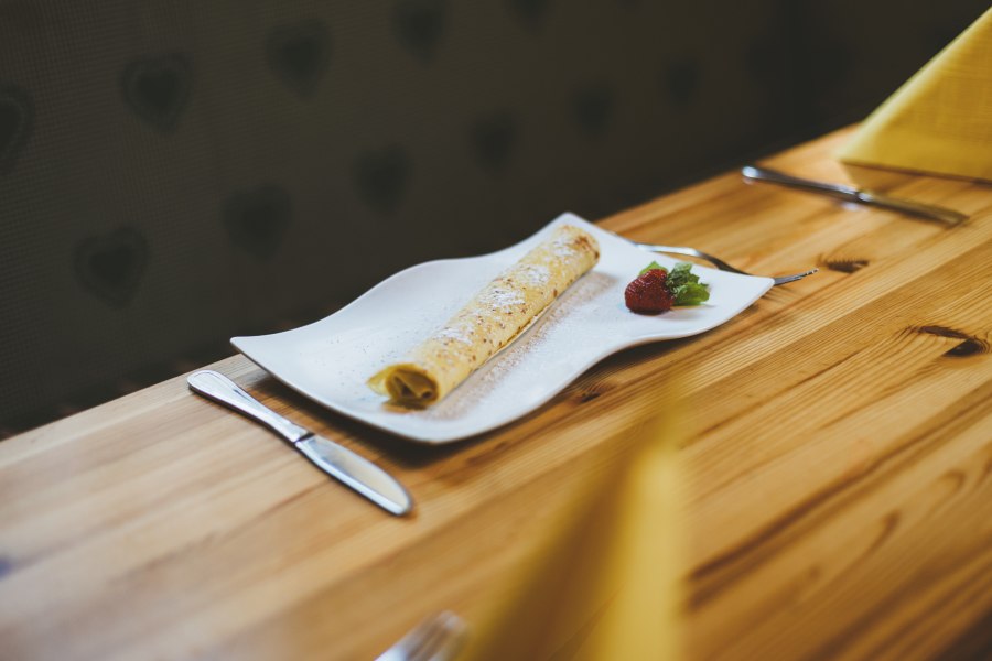 Eine Palatschinke auf einem weißen Teller mit Erdbeere und Minze, auf einem Holztisch serviert.