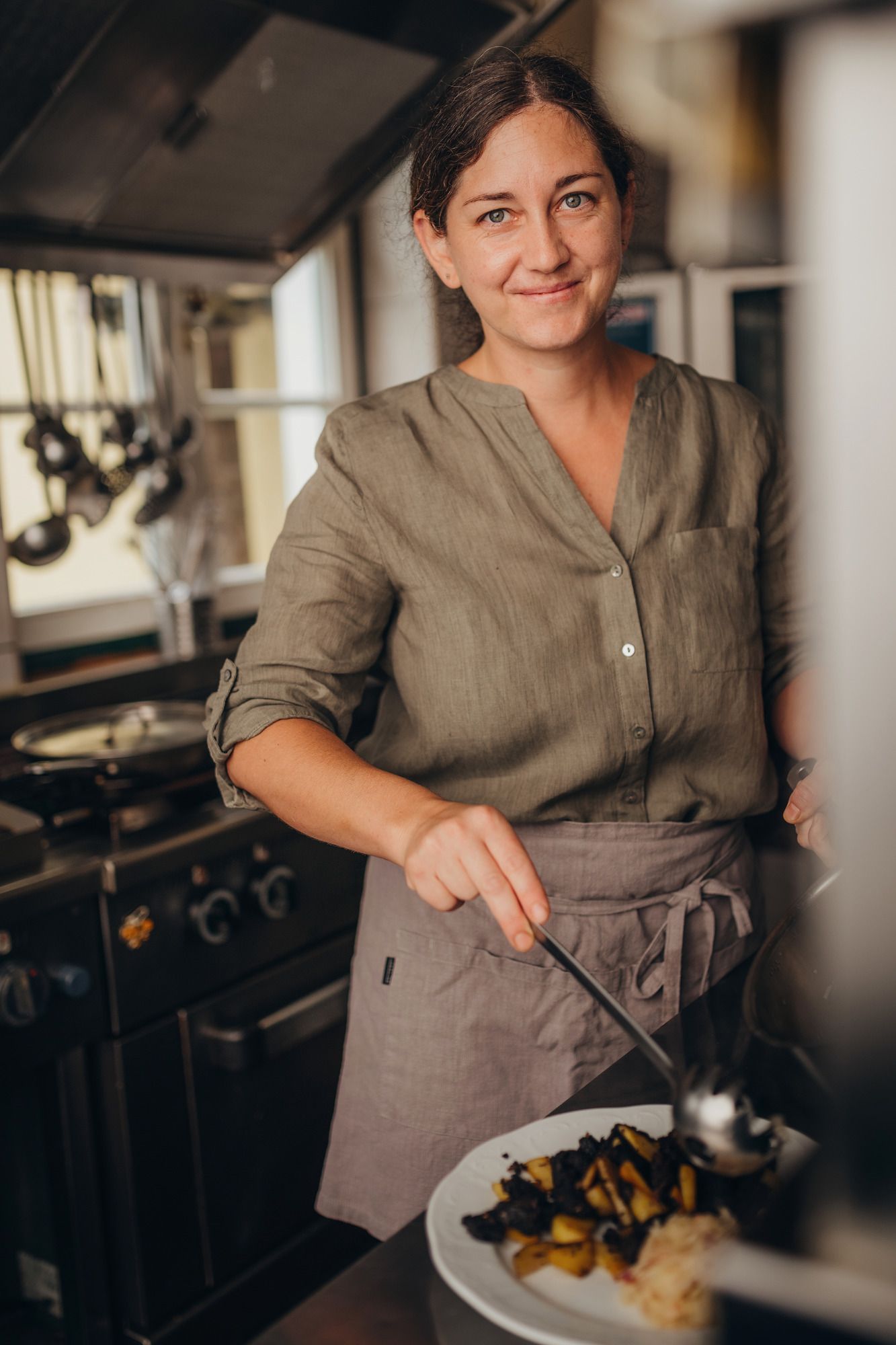 Woman in a kitchen serving food on a plate.