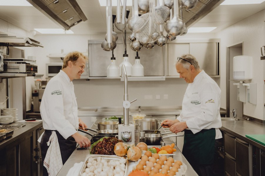Zwei K&ouml;che in einer professionellen K&uuml;che, die gemeinsam kochen. Auf dem Tisch liegen Gem&uuml;se und Eier.