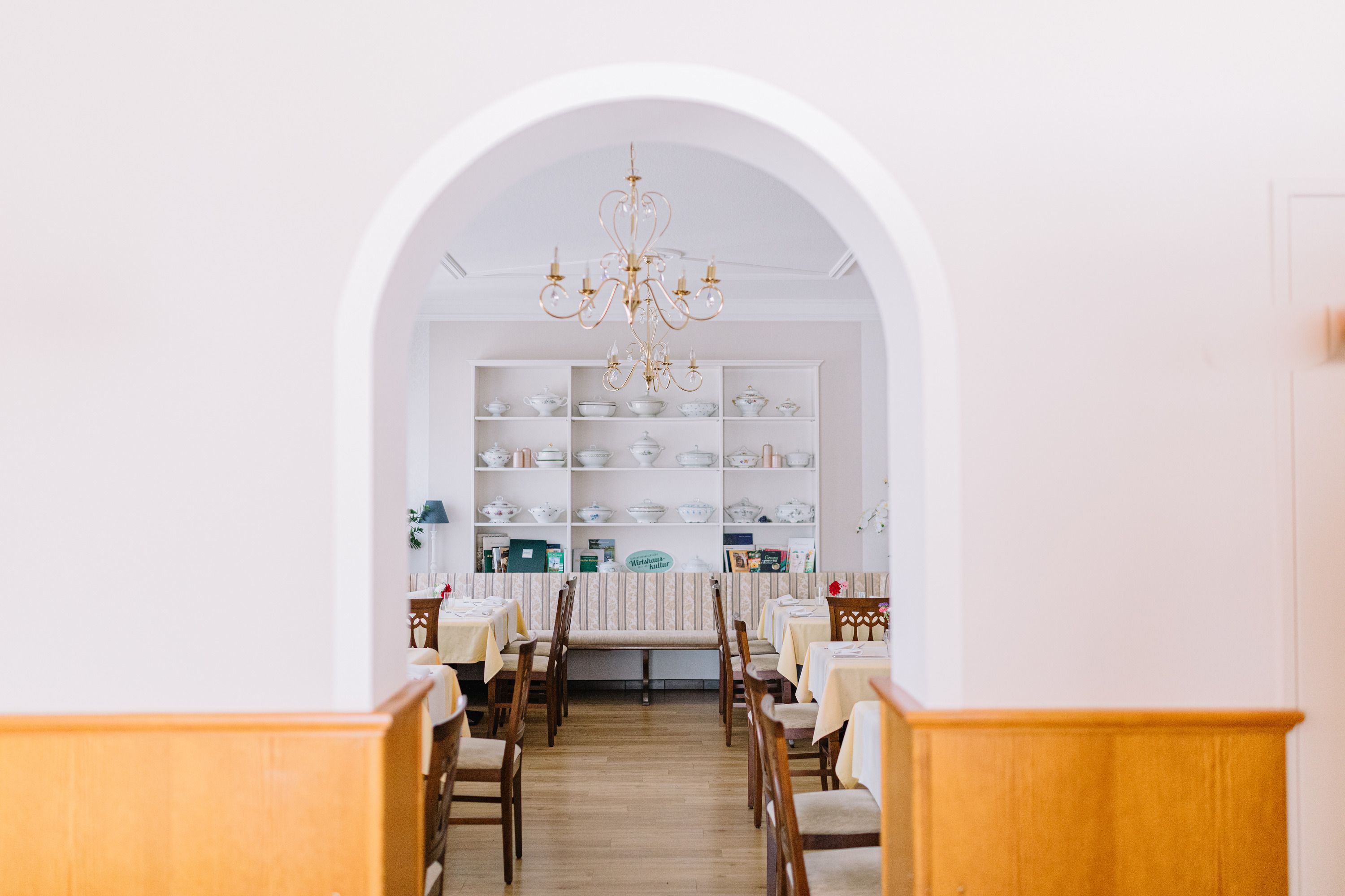 Innenansicht eines traditionellen Wirtshauses mit gedeckten Tischen und einem Kronleuchter.