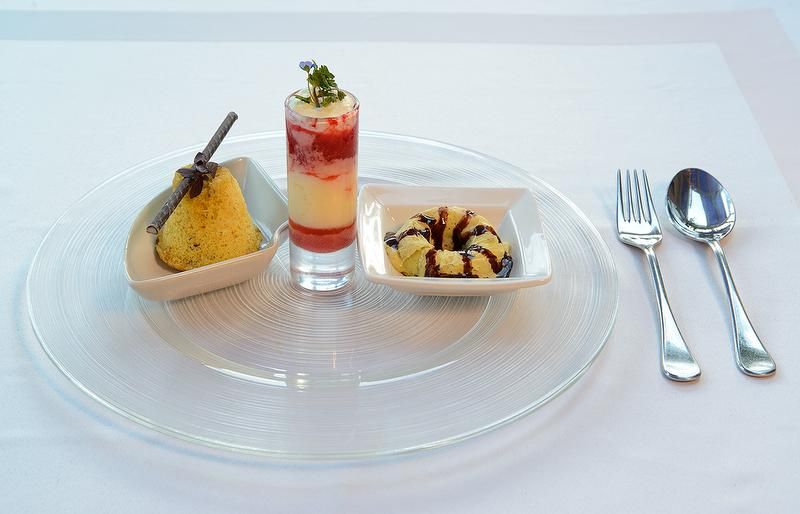 Drei Desserts auf einem Teller: ein Kuchen, ein Schichtdessert im Glas und ein kleiner Kuchenring, daneben Besteck.